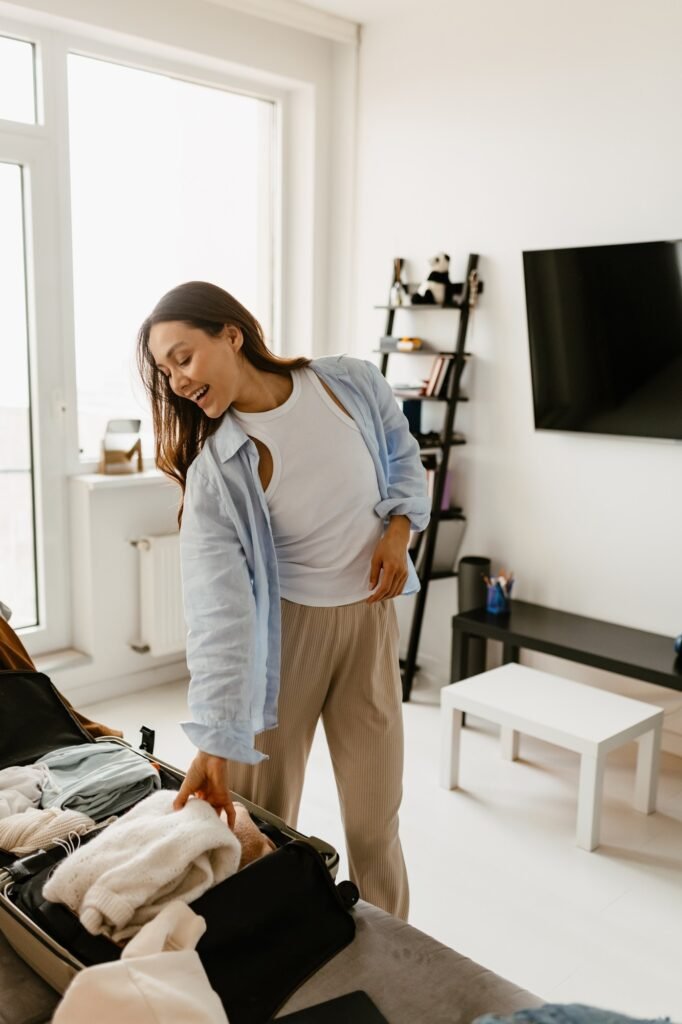 Woman standing and smiling while packing things into a suitcase in living room