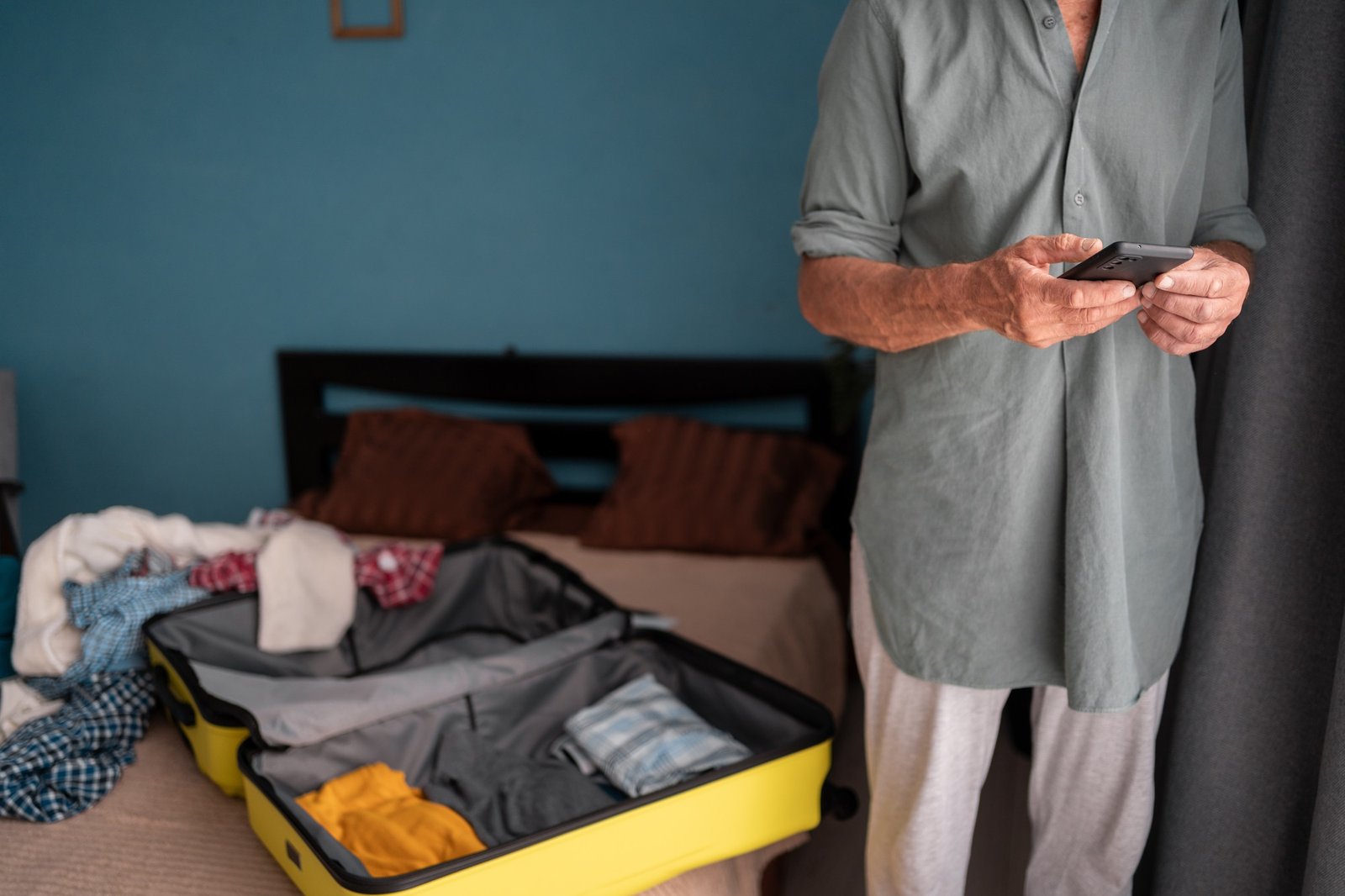 Senior man packing his luggage for upcoming trip, using the checklist on smartphone.